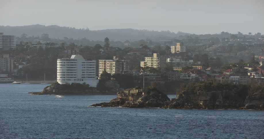 Waves splash up on the rocks with hotels and buildings along the coast