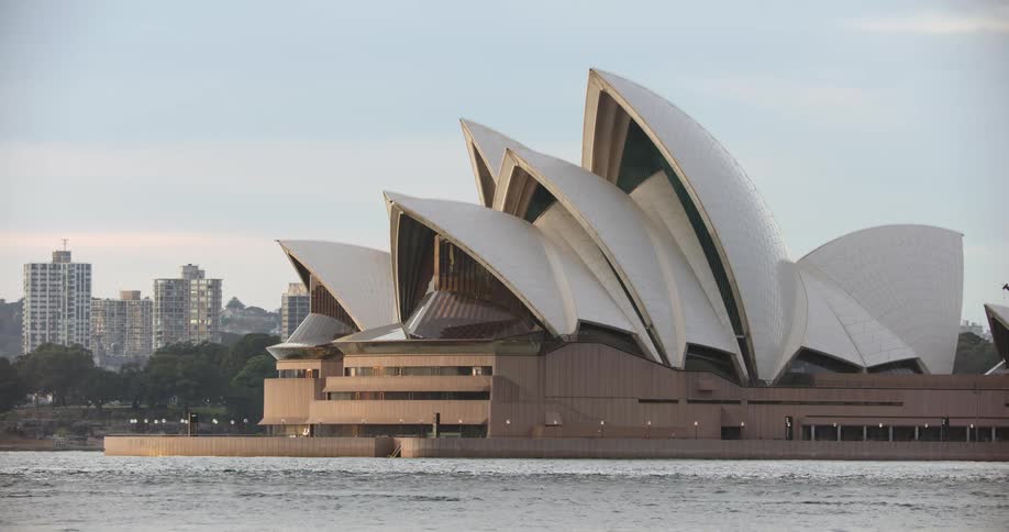 The sydney opera house with small waves and city buildings behind