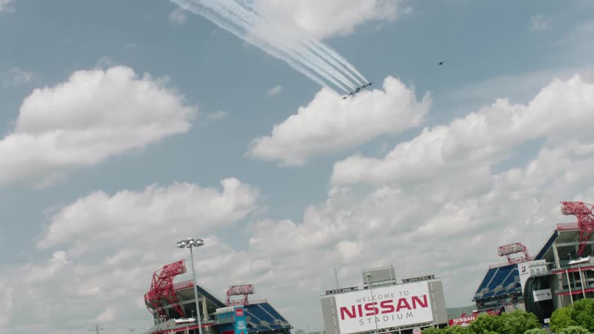 A large crowd watches airplanes fly in a formation