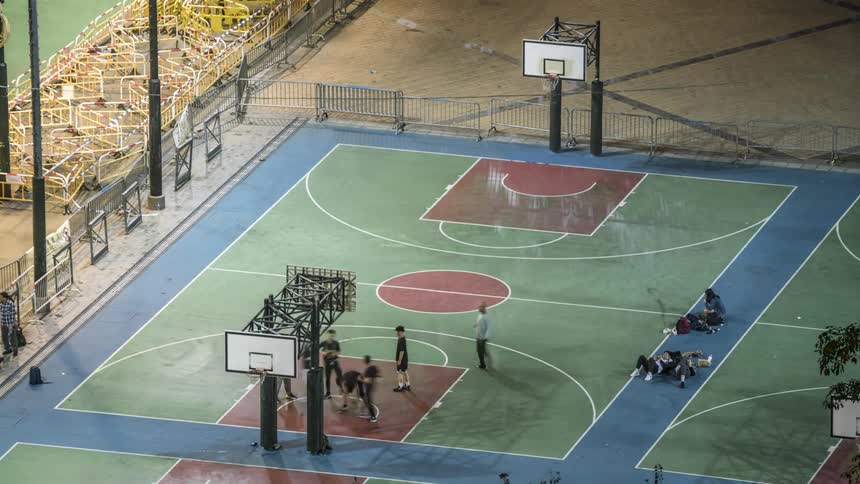 People sit and lie next to the outdoor basketball court watching others play