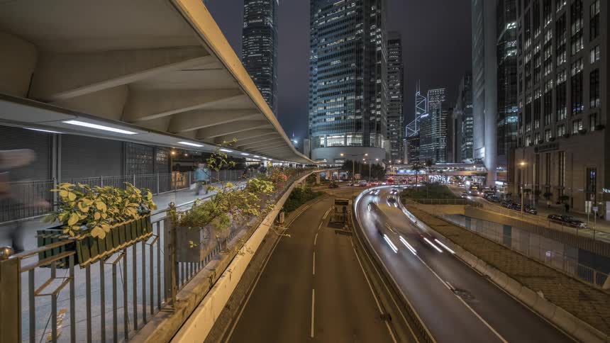 Vehicles drive on the highway next to the tall and illuminated buildings at night in the city