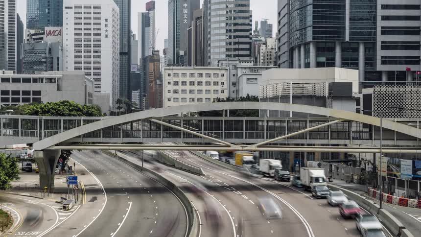 People walk across a pedestrian bridge over a city highway with a lot of traffic