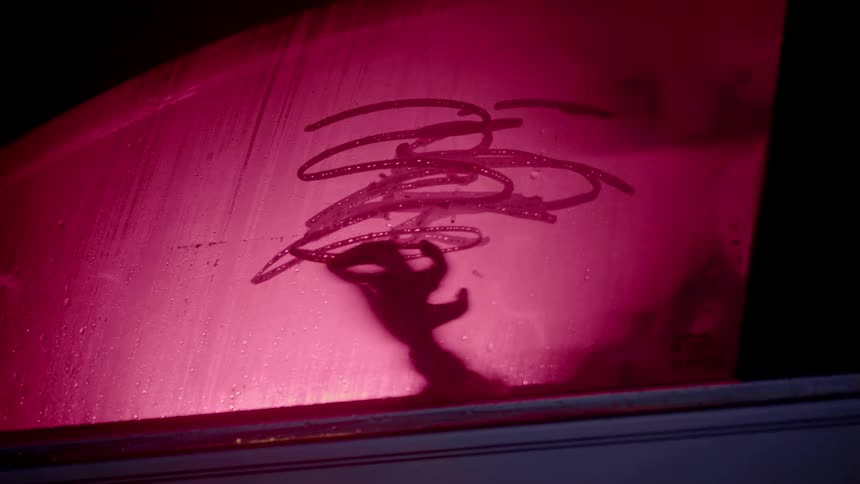 A person rubs their finger on the condensation of a car window