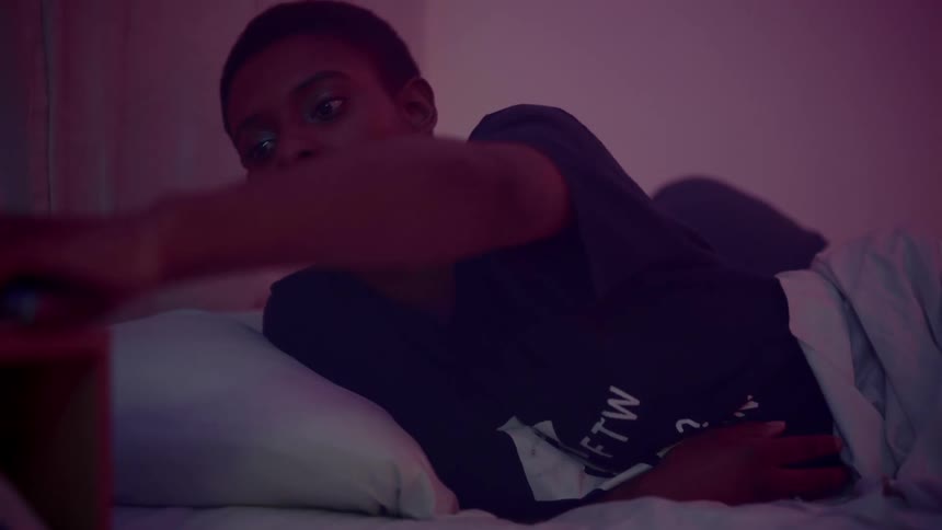 A woman leaning up in bed looks at her smartphone then places it down in frustration before lying on her back in bed