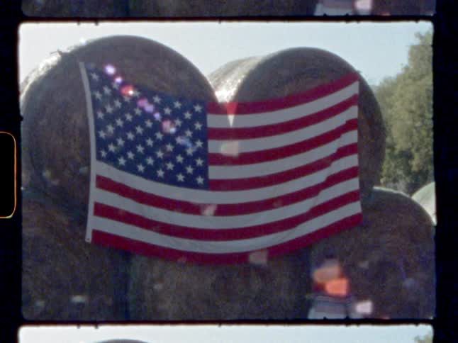 A young boy walks past hay bales with an american flag on them