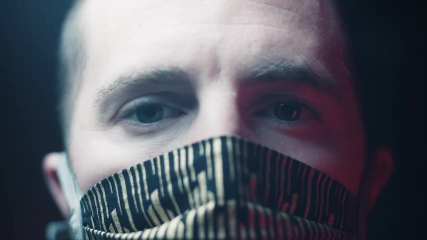 A man wearing a patterned face mask while looking directly into the camera