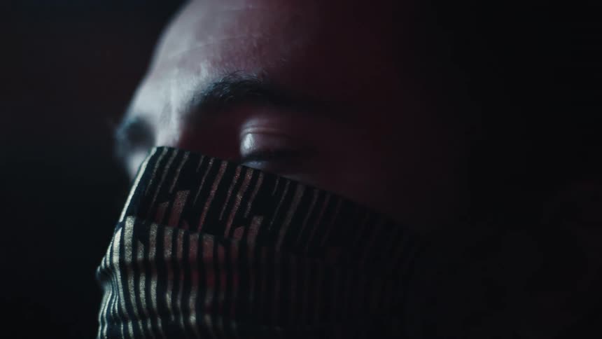 Side profile of a man wearing a face mask against a dark background