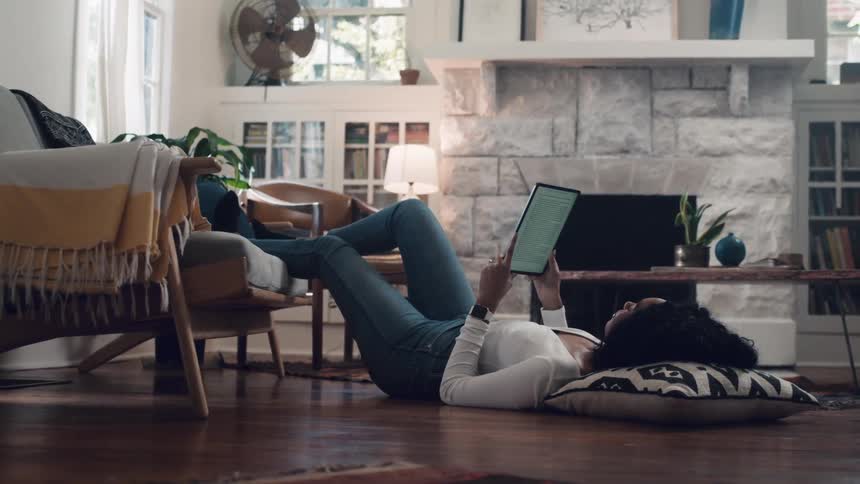 A young girl lies on the floor and reads on a tablet