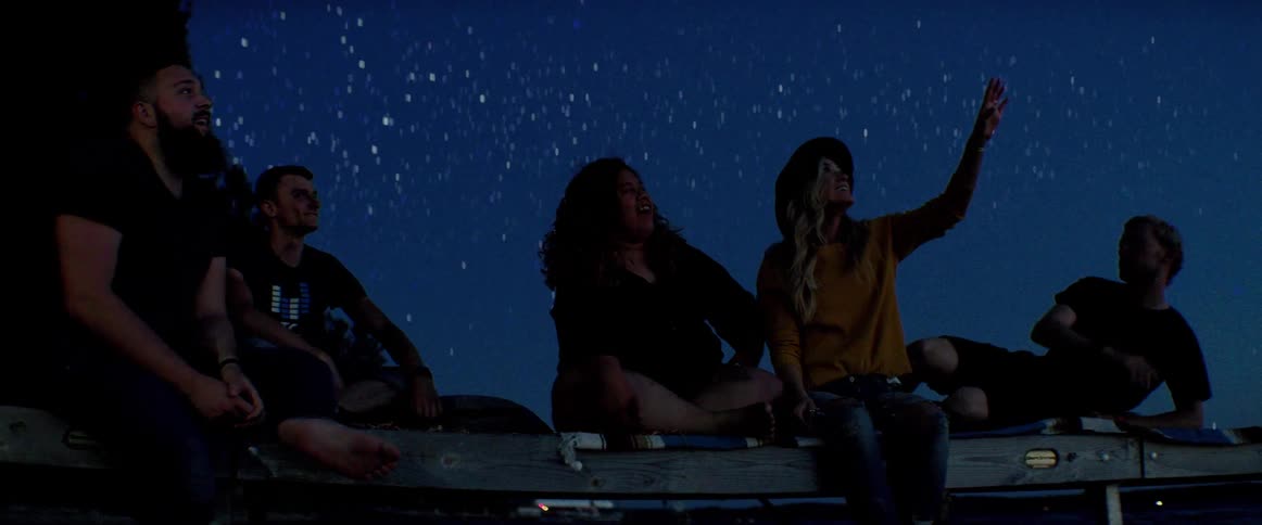 A group of friends sit on top of a camper and watch the stars at night