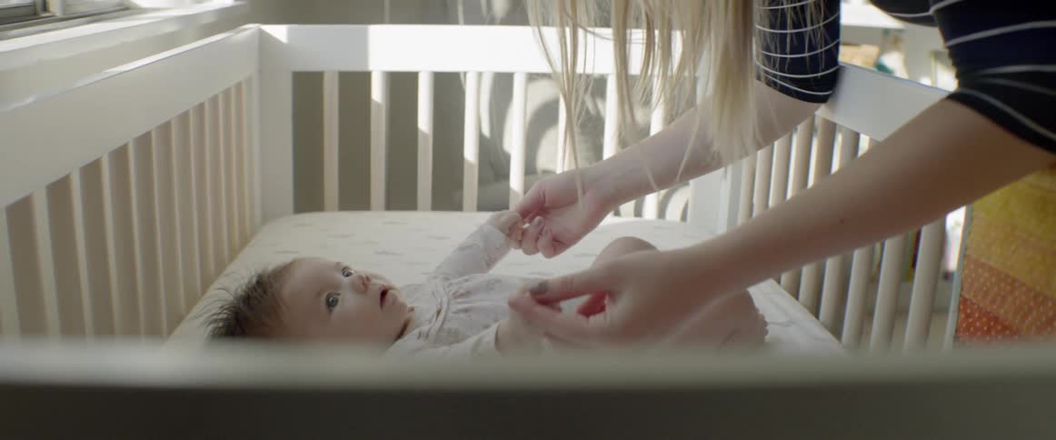 Mother leaning over crib and playing with baby daughter