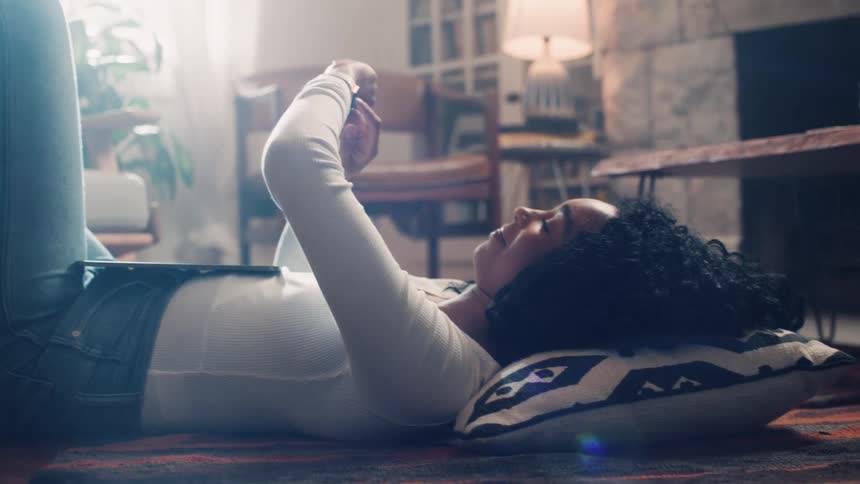 A woman lays on the floor scrolling on her watch