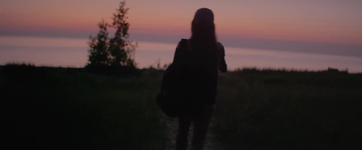 A woman hikes along a trail toward a body of water at sunset