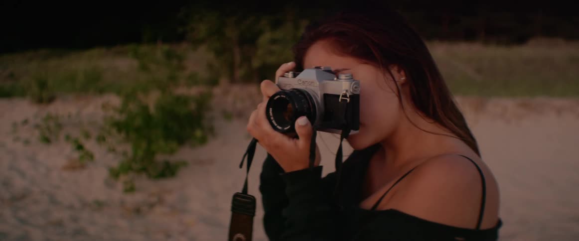 A woman with a camera taking a photo on a beach