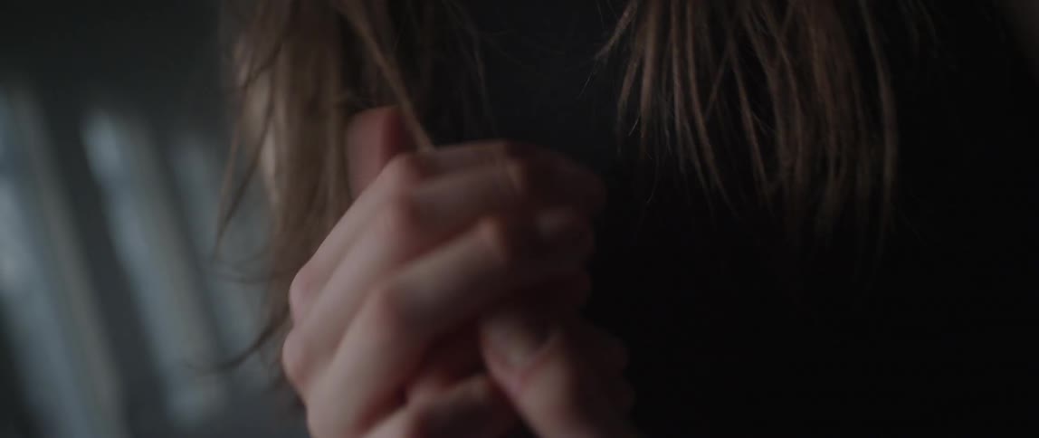 A woman brushing her hair away from her face and clasping her hands