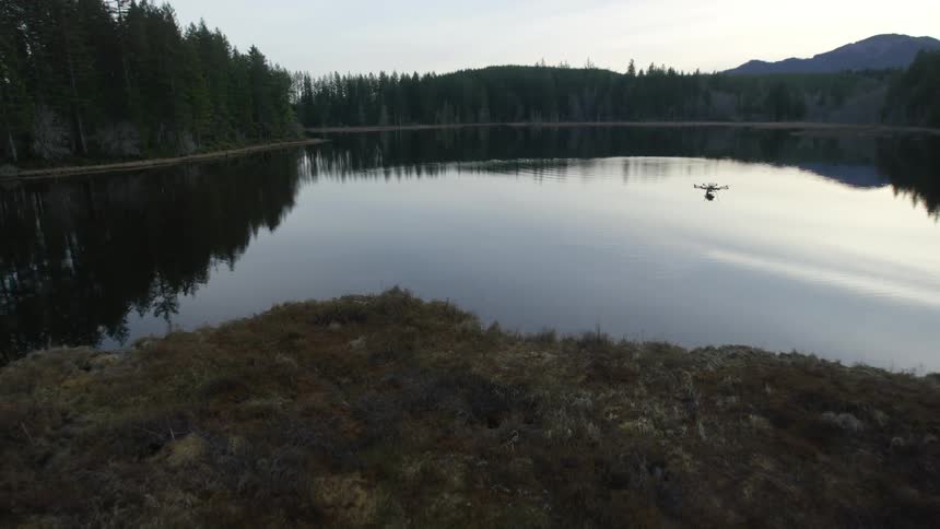 A drone hovers over a calm lake in the mountains