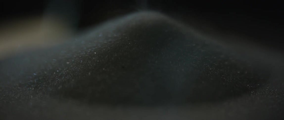 Dark grains of sand are poured onto a mound