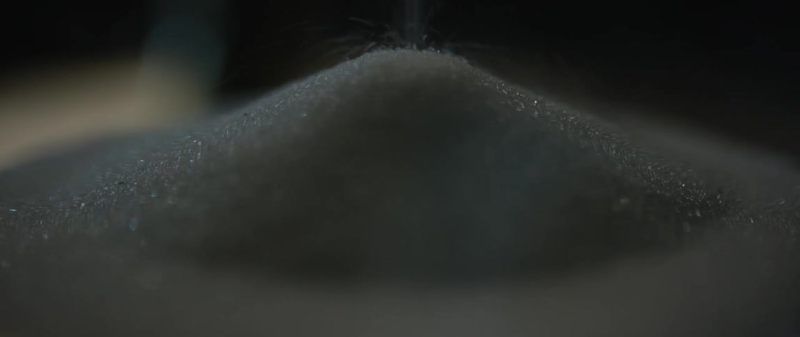 Black sand is slowly poured and forms a small peak