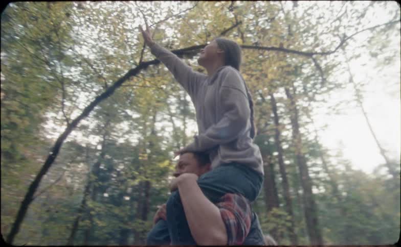 A man holds his teenage daughter on his shoulders to reach a tree