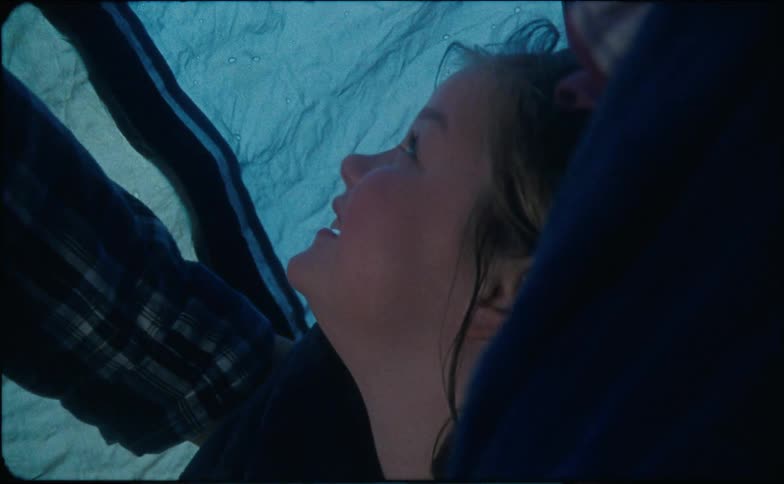 Parents wrap a little girl in a blanket in a tent as the rain falls outside