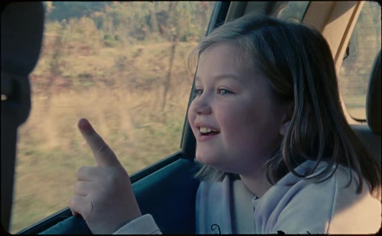 A girl stares out the window of a car while driving down a road