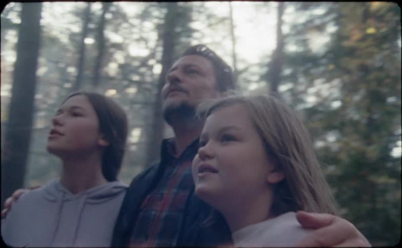 A dad walks in the woods with his arms around both of his daughters