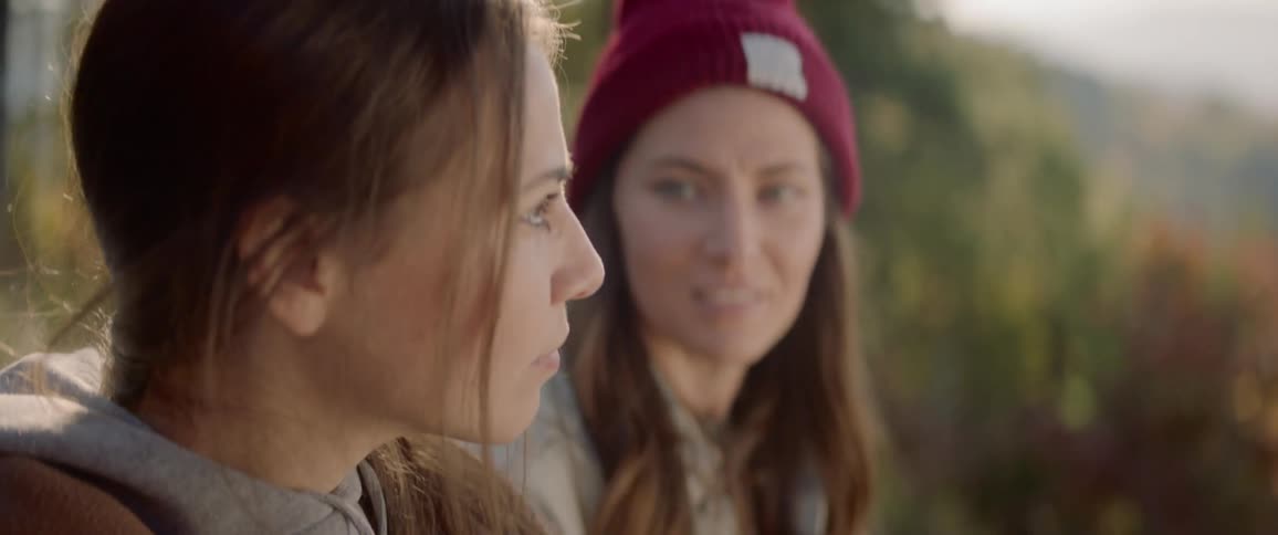 Two women smile and talk near the trees