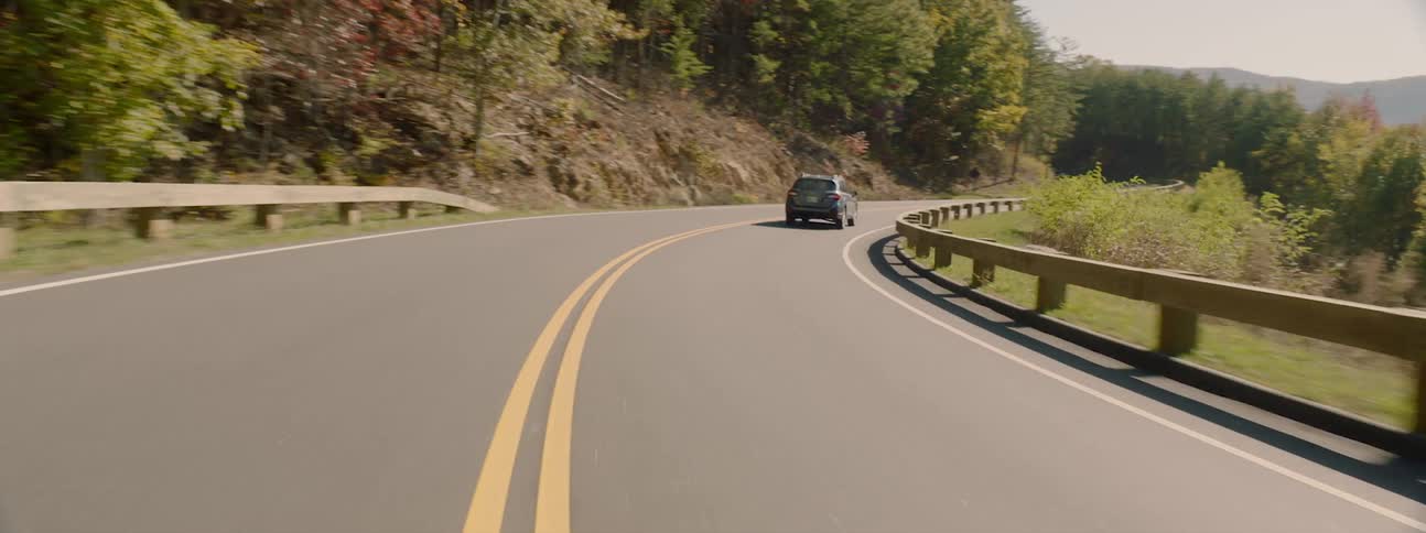 Vehicle travels down a winding road near the trees