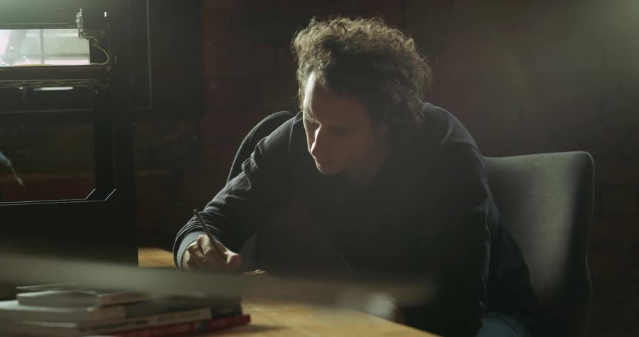 A man sits at a desk and looks at something and takes notes