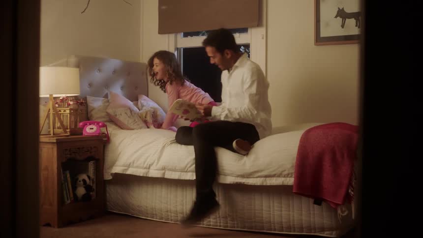 A dad carries a book and follows his daughter to her room to read her a bedtime story
