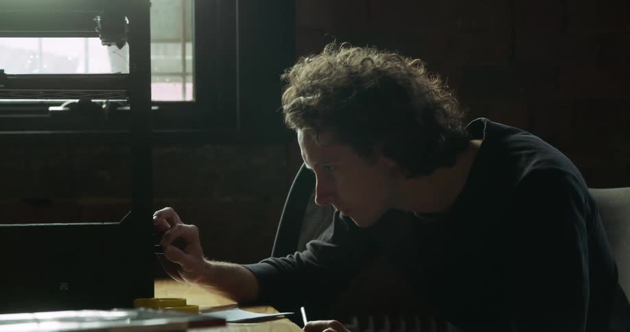 White man studying a 3d machine while writing down on his notebook