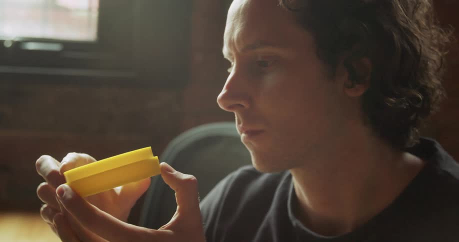 A man taking a yellow plastic cylinder from a 3d printer and looking at it