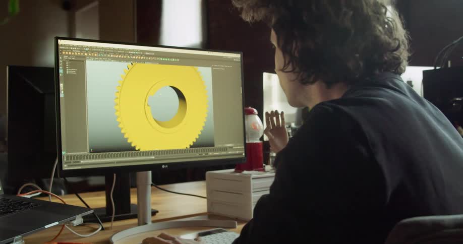 A man sits at a computer holding a gear and looking at a computer model of the same gear