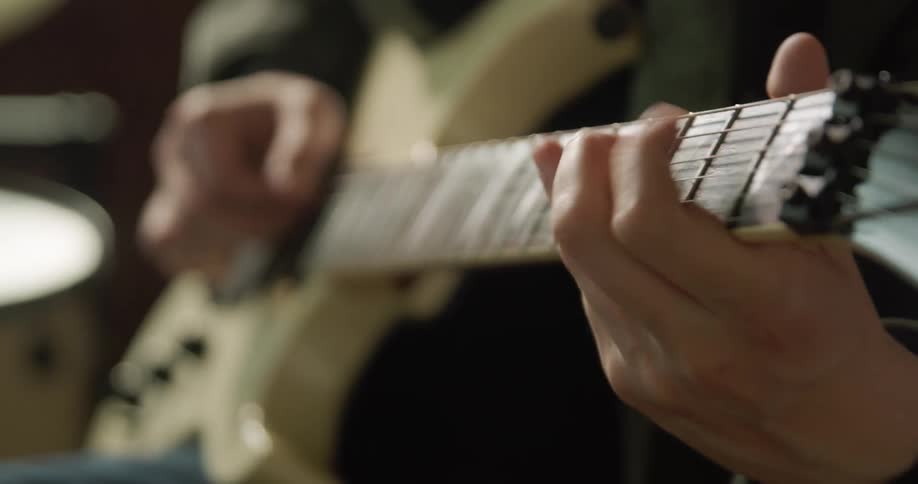 A man sitting down indoors while playing a guitar