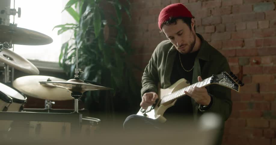 Man sitting playing guitar in front of his drums set