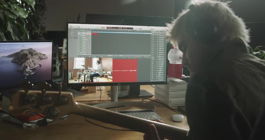 A man sits in front of a computer playing an electric guitar