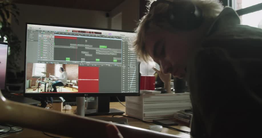 A man uses a computer to record himself playing guitar alongside a video of a man playing the drums