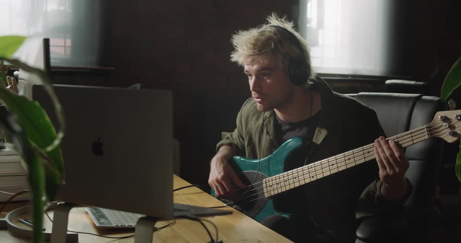 Man sitting at the desk records bass guitar on a pc computer in the office