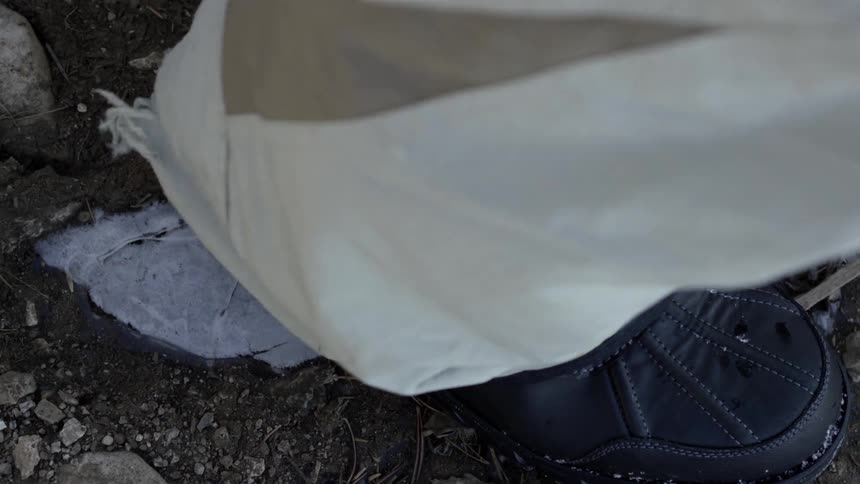 A hiker steps on and breaks a small section of ice on the ground