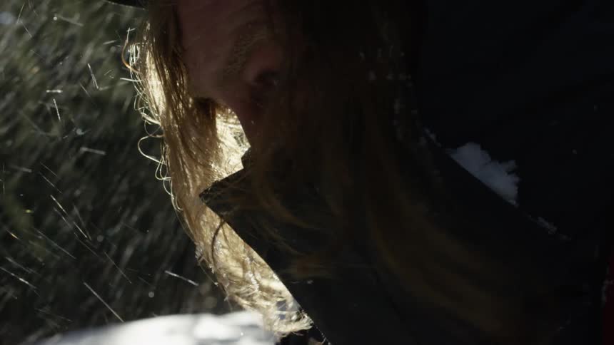 A mans face covered with a overcoat as snow blows behind him