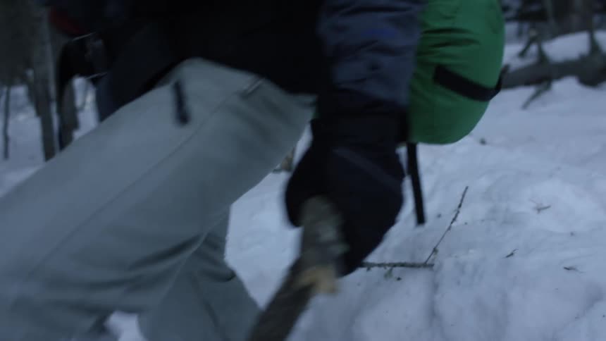Man breaks stick across leg in snow covered forest