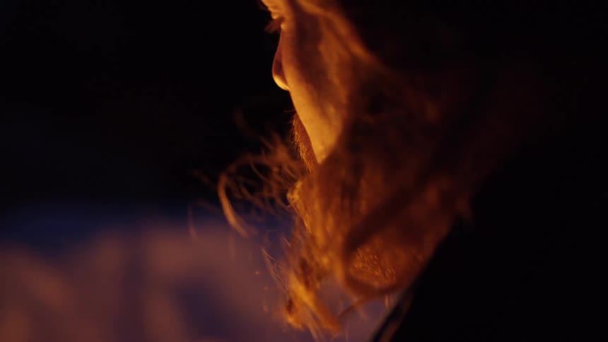 Yellow light flickers against a mans face as he watches a fire
