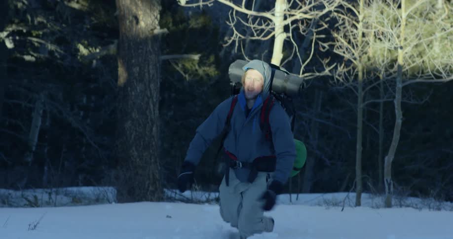 A man struggles walking through the snow coming out of a woods area