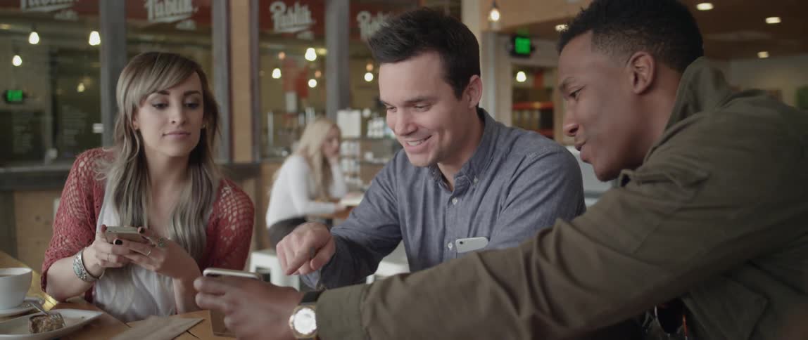 A group of people smile and laugh while looking at a smartphone in a restaurant