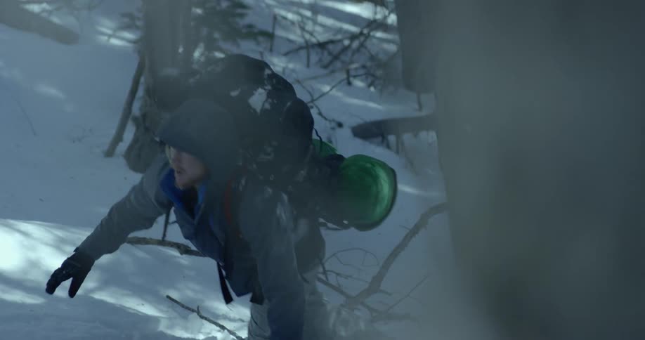 A man hikes through a snow filled woods area with a large hiking backpack