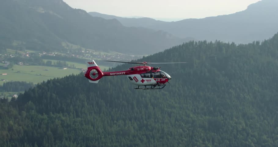 Helicopter flies backward over mountain forest near town nestled in valley
