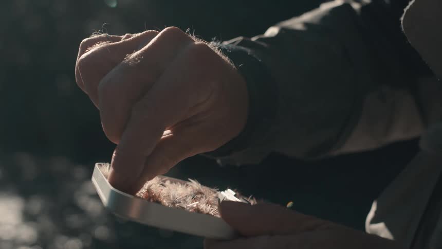 A fisherman holding a case of fishing flies near the river selects one