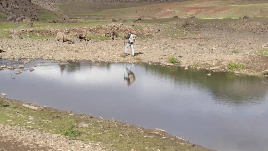 A backpacker hikes past a small pond