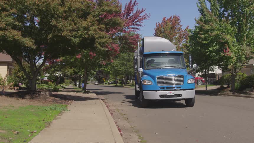 A trash collection truck stops in front of a home and pick up the trash can to dump in the truck