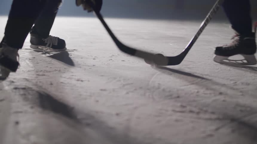 Two men are playing ice hockey in a vacant sports stadium lit by only one large light