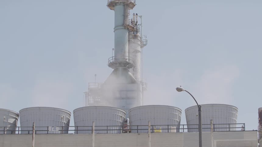 A factory with smoke coming out of the chimneys with a truck driving by in the foreground